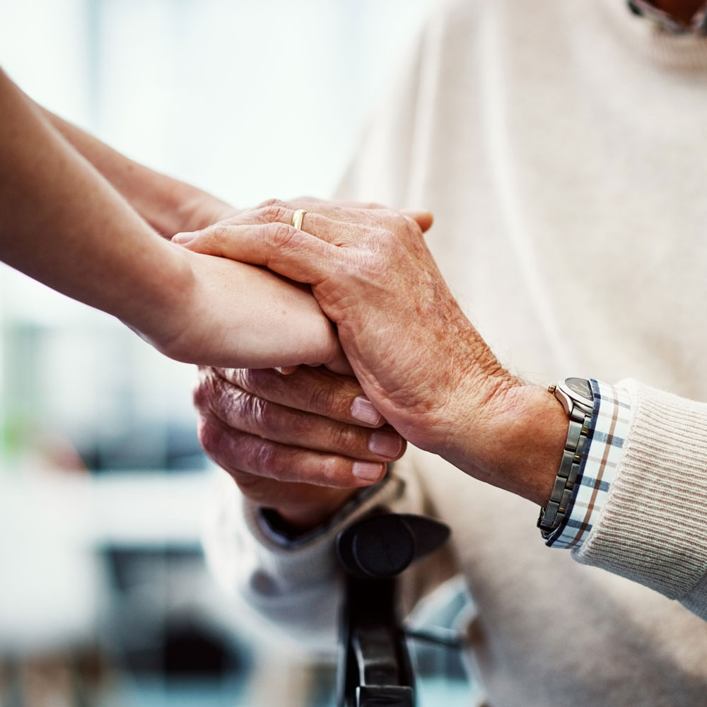 close-up of a senior woman's hands clasping those of her caregiver