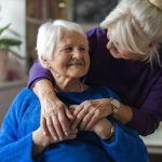 woman smiling and hugging her senior mother from behind