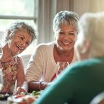 senior women laughing and talking at a table while drinking wine