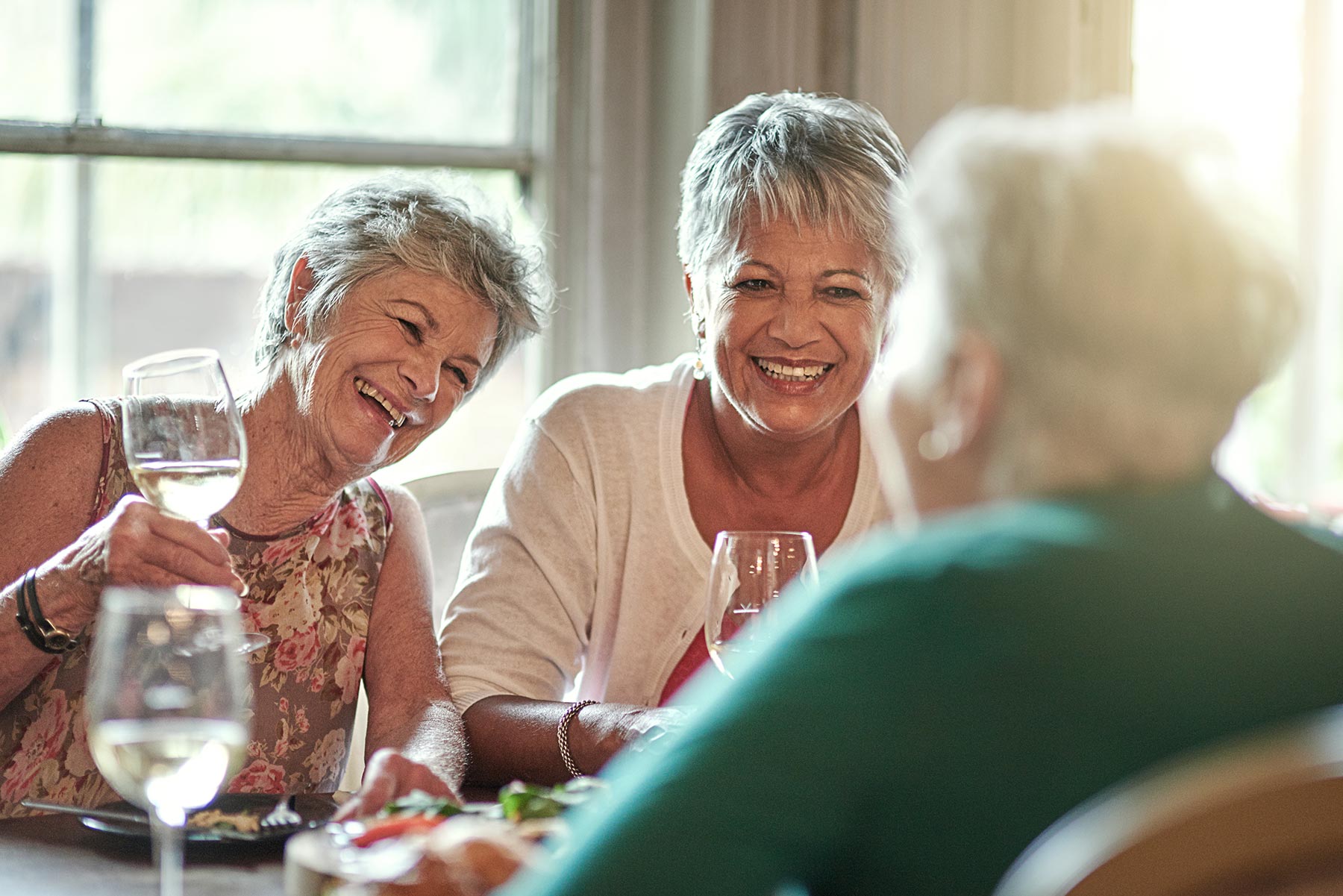 senior women laughing and talking at a table while drinking wine