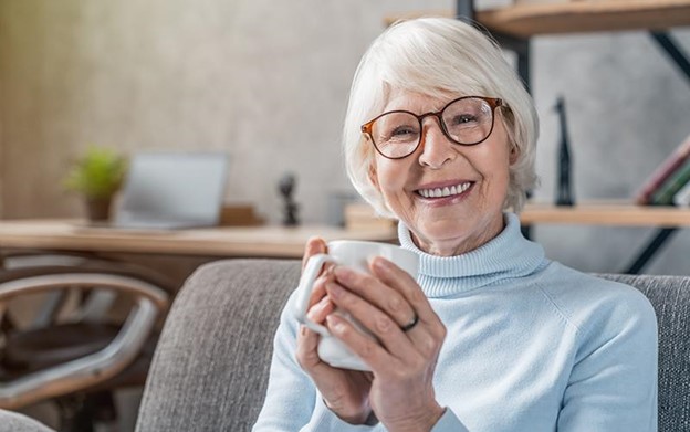 senior woman sitting in her living room smiling and drinking coffee