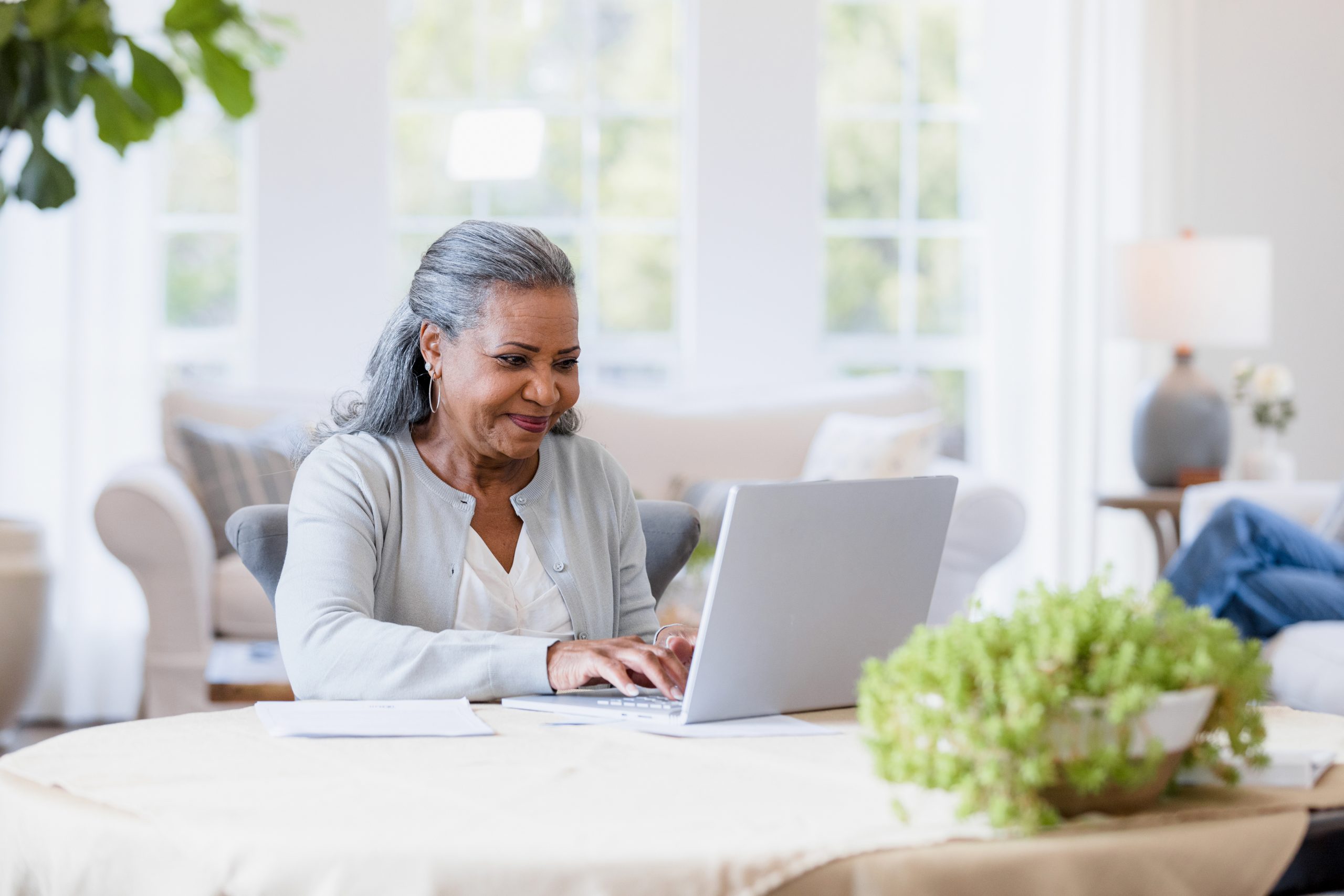 senior woman sitting in her kitchen looking at her laptop